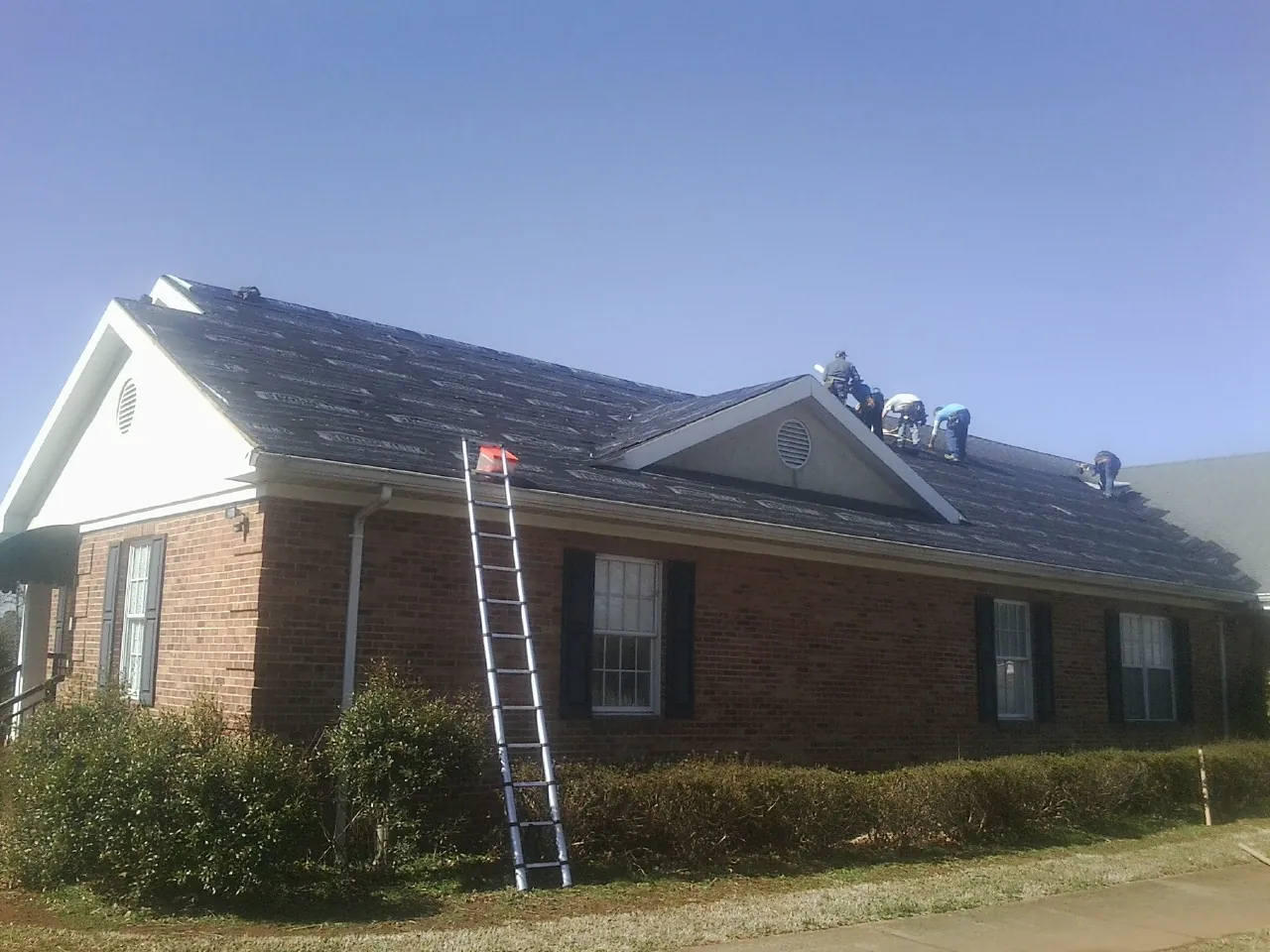 Crew tearing shingles off a brick ranch roof with a ladder set — Emergency Roof Repair work by our crew in Beardsley