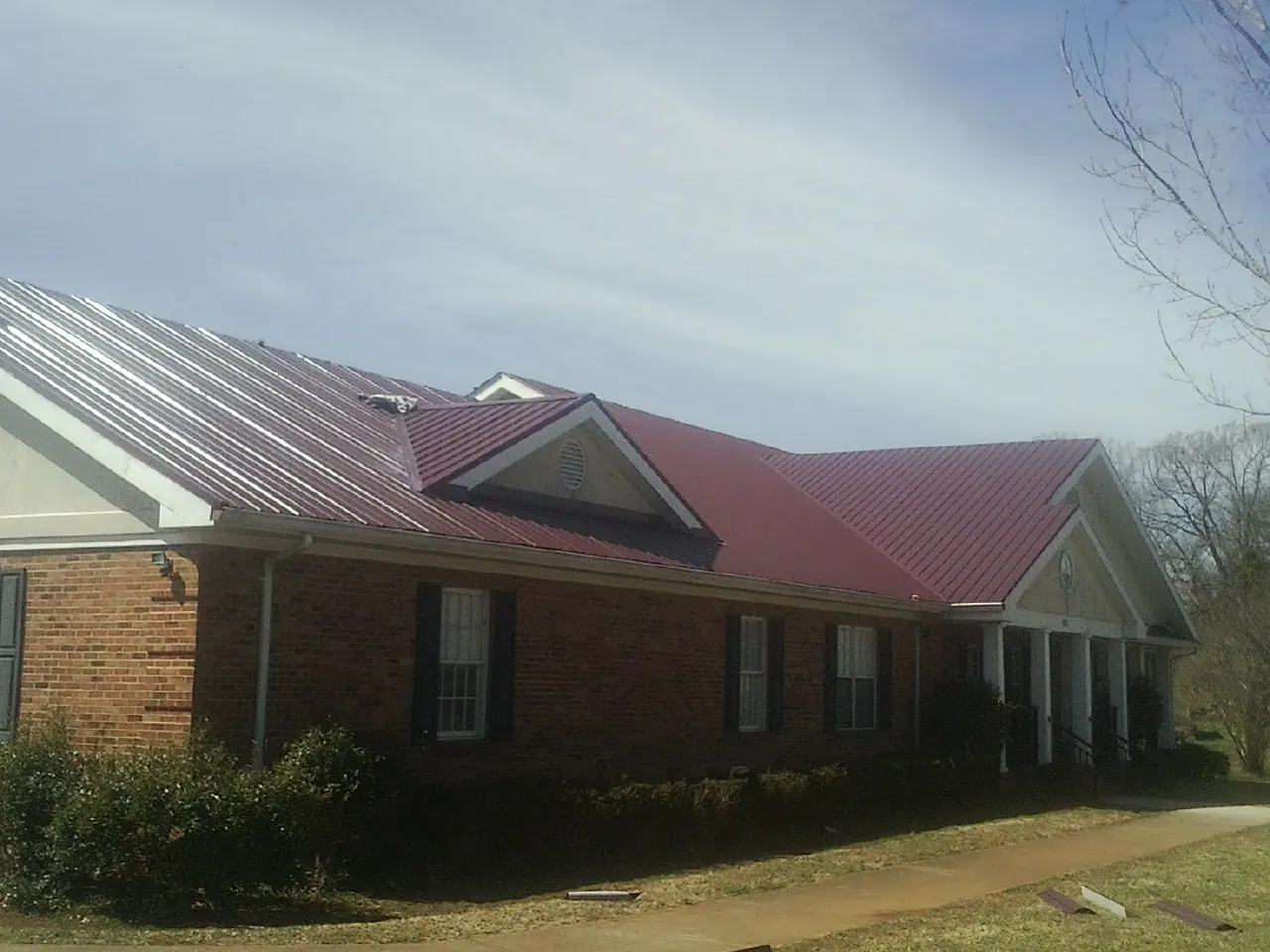 Red metal roof with gabled entries on a long brick building, from a Hail Damage Roof Repair job in Beardsley