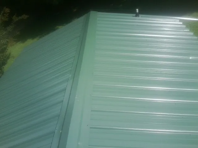 New green metal panels meeting at the ridge of a roof — Flat Roof Repair work by our crew in Beardsley