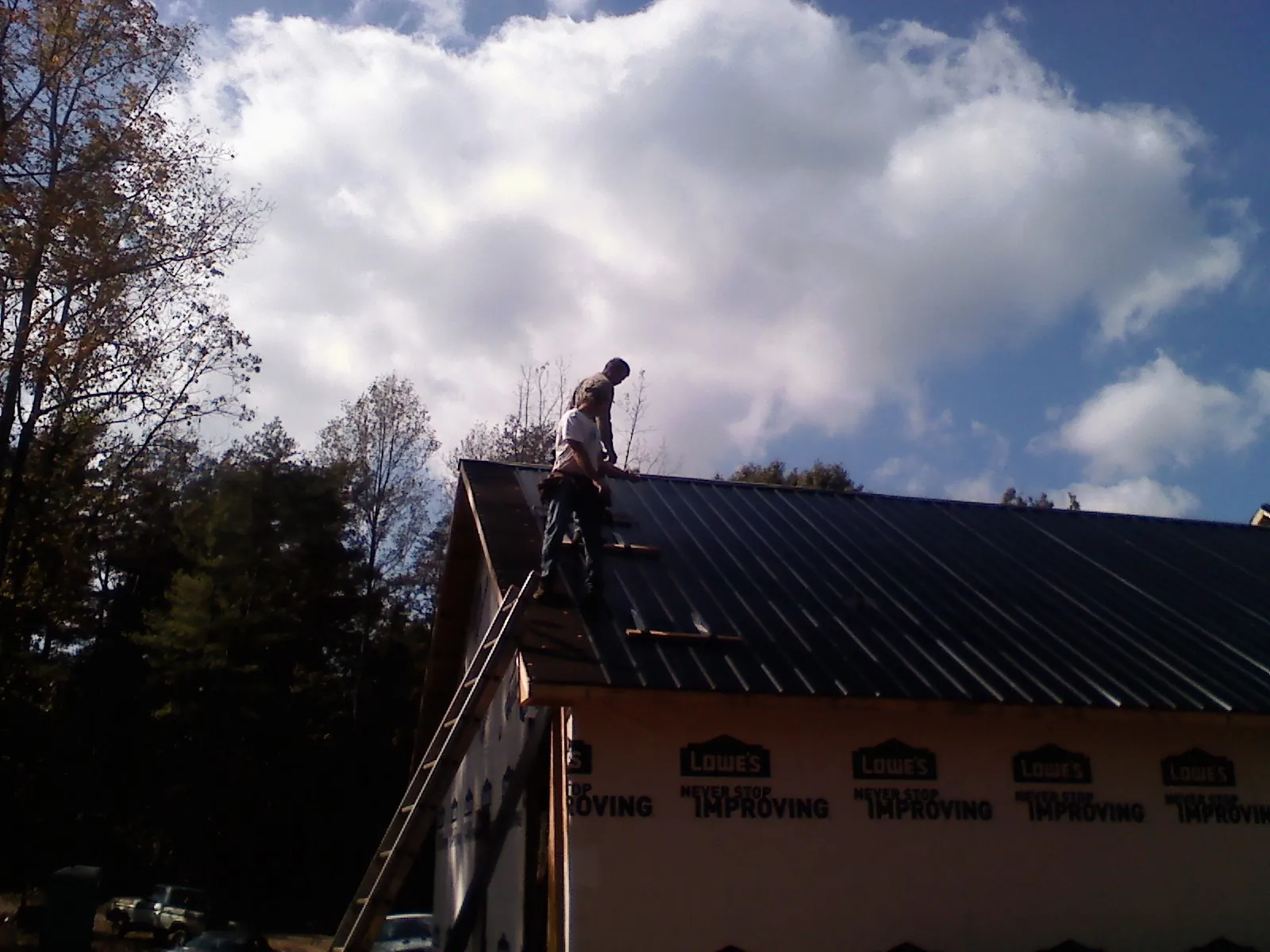 Roofer fastening dark metal panels high against a cloudy sky, from a Roof Inspection job in Beardsley