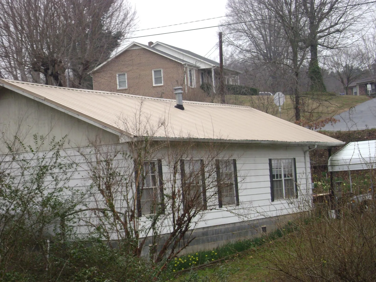 Tan metal roof on a white sided house set into a hillside — Commercial Roofing by Roofing Brothers in Beardsley